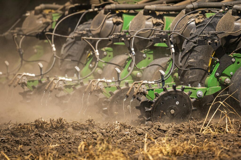 Close-up of modern agricultural machinery sowing seeds on a dusty field.